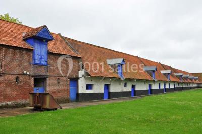 Tour en briques avec toit en ardoise, entourée de bâtiments ruraux et d'arbres, sous un ciel dégagé.