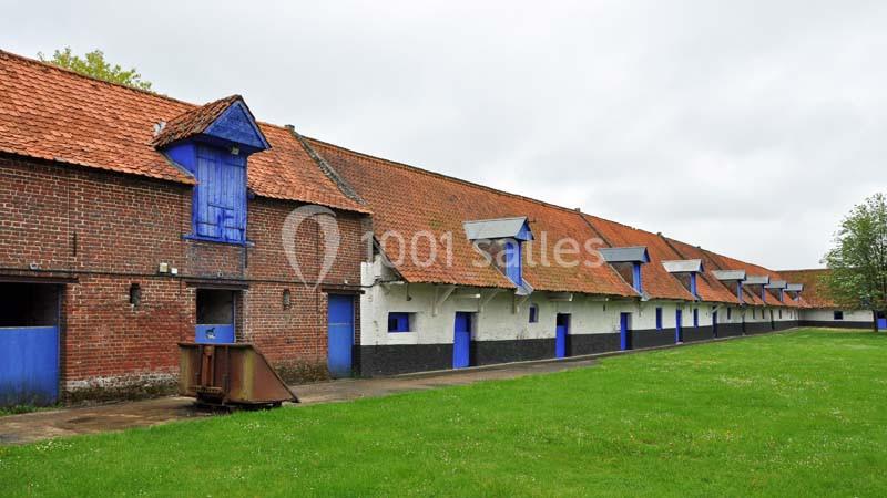 Bâtiments agricoles en briques et enduits blancs avec toits en tuiles rouges, alignés sur une pelouse verte.