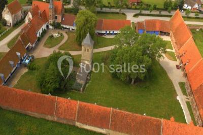 Tour en briques avec toit en ardoise, entourée de bâtiments ruraux et d'arbres, sous un ciel dégagé.