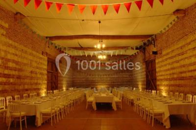 Tour en briques avec toit en ardoise, entourée de bâtiments ruraux et d'arbres, sous un ciel dégagé.