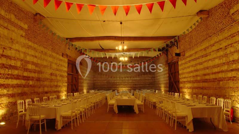 Salle de réception en briques avec tables dressées et guirlandes colorées suspendues sous un plafond blanc.