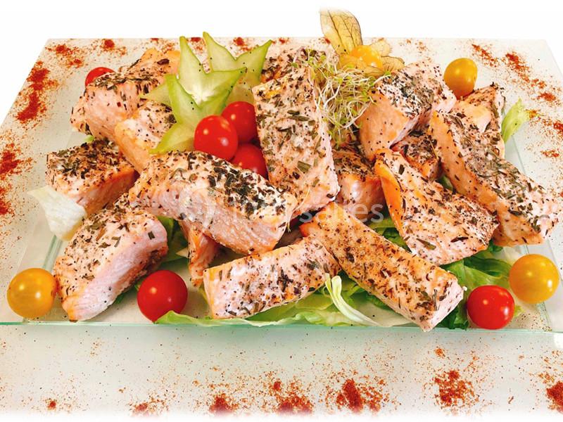 Assiette de morceaux de saumon grillé aux herbes, accompagnés de tomates cerises, salade et décorations végétales.