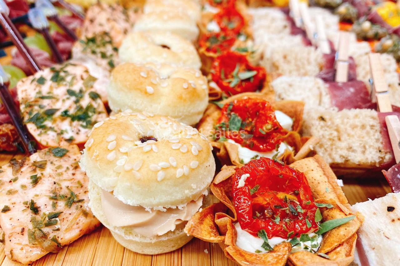 Plateau de bouchées variées comprenant mini-burgers, tartelettes aux tomates séchées et autres amuse-bouches.