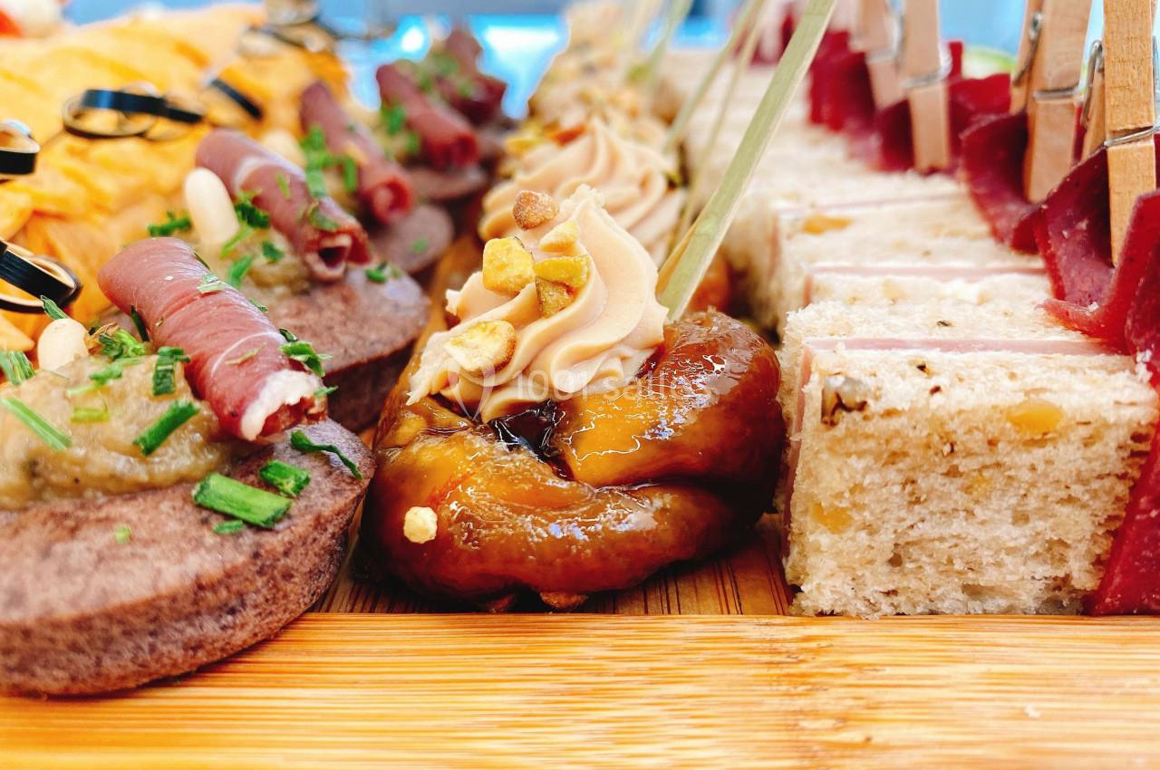 Assortiment de bouchées apéritives variées disposées sur un plateau en bois, incluant toasts, viandes et garnitures.