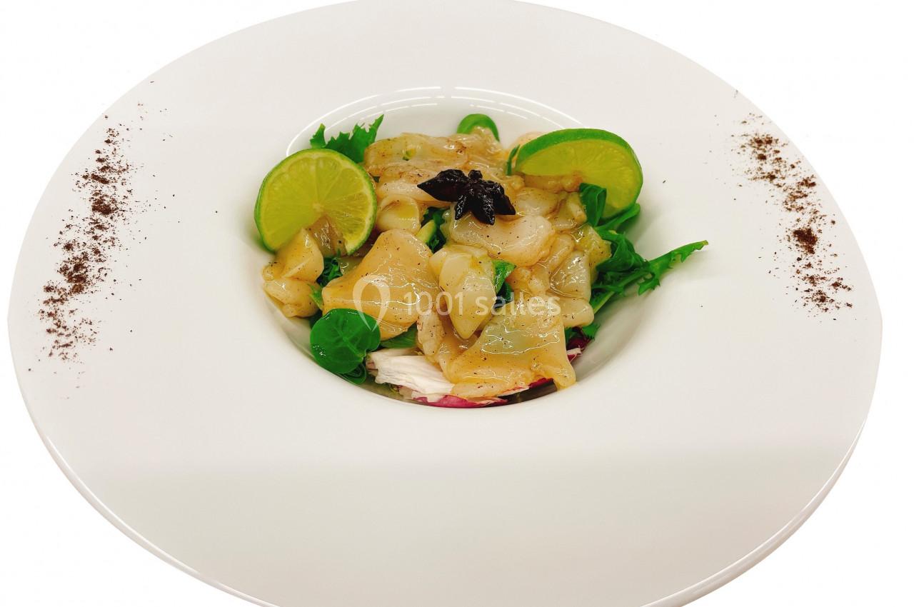 Assiette de carpaccio de Saint-Jacques avec tranches de citron vert, salade verte et décoration de poudre épicée.