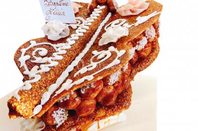 Gâteau à trois étages décoré de motifs dorés, plumes blanches et perles, avec une inscription d'anniversaire.