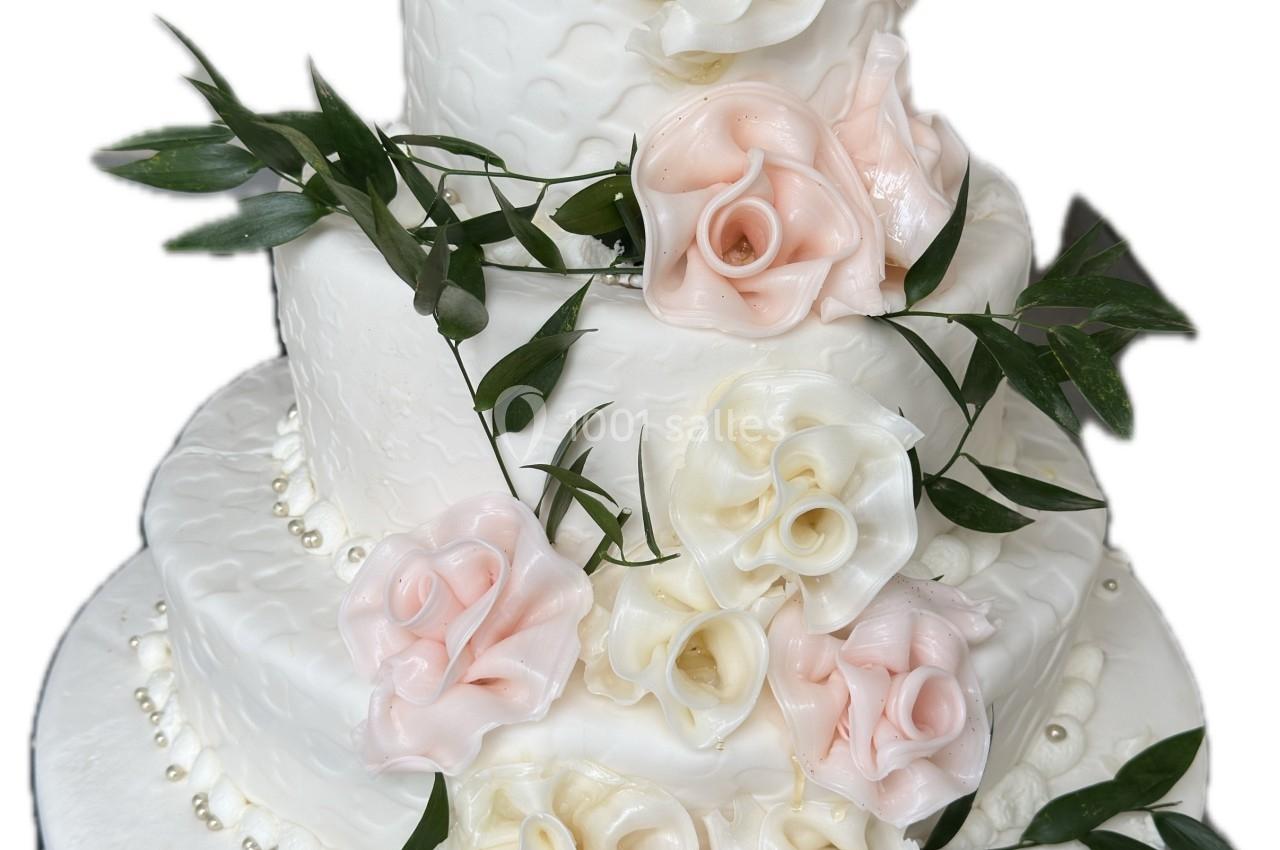 Gâteau de mariage à quatre étages décoré de roses en sucre blanches et roses, avec des feuilles vertes.