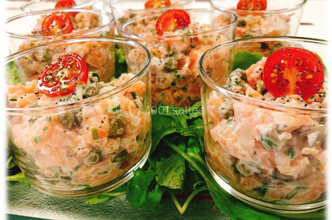 Verrines de tartare de saumon avec câpres, herbes fraîches et rondelles de tomate cerise, servies sur un lit de roquette.