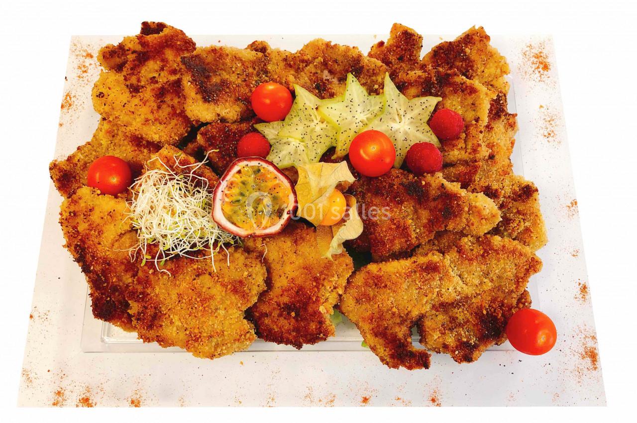 Assiette de filets panés garnie de fruits exotiques, tomates cerises et germes, présentée sur un plat blanc.