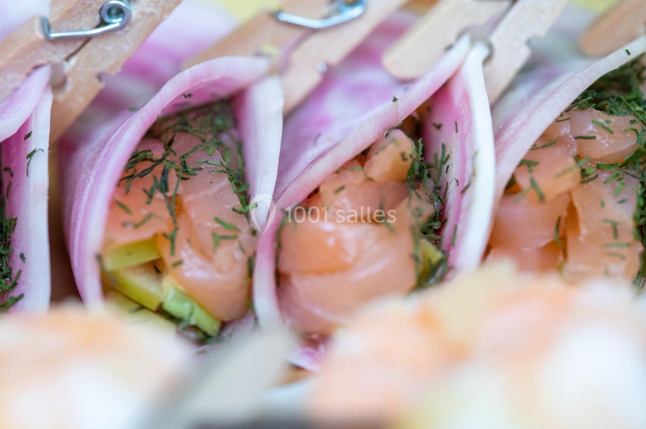 Tranches de saumon, avocat et aneth présentées dans des feuilles colorées, fixées avec des pinces en bois.