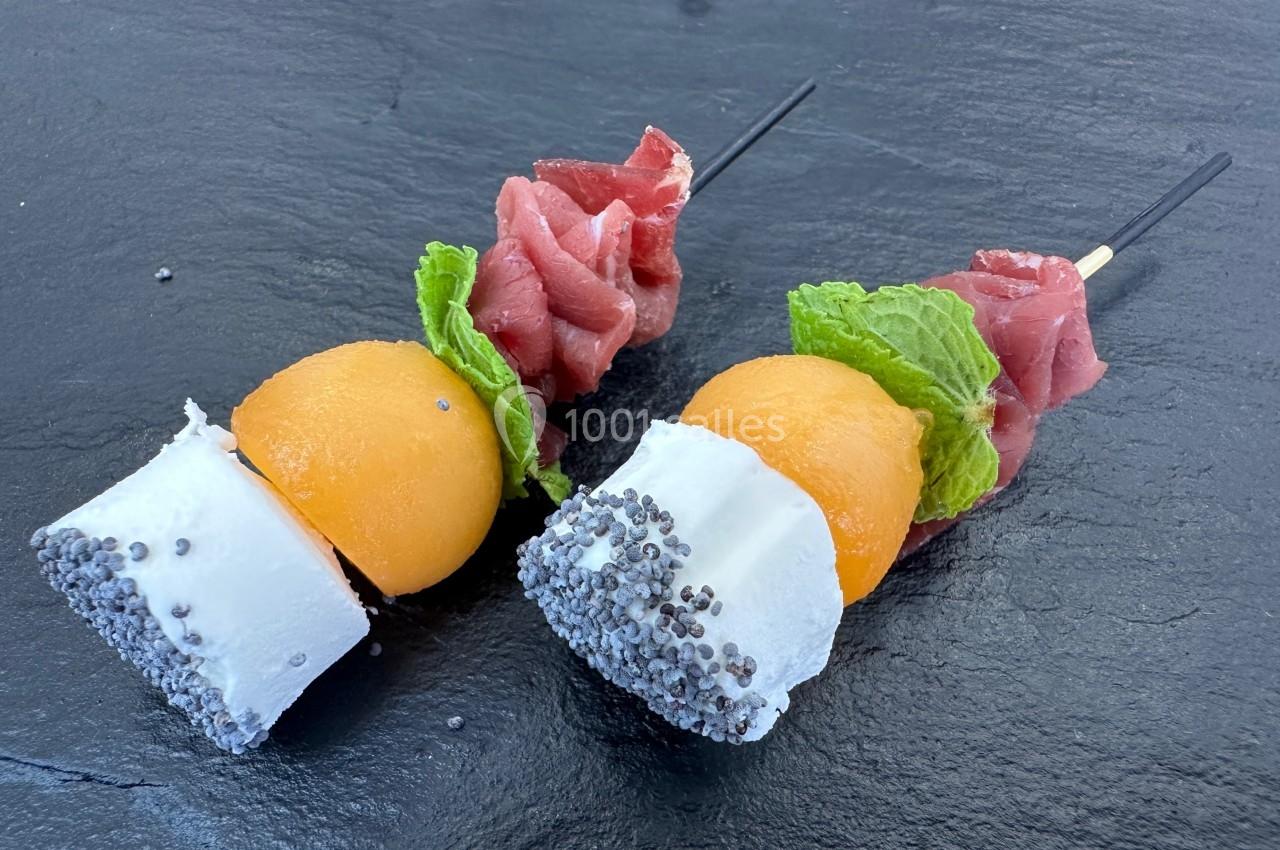 Brochettes composées de billes de melon, fromage enrobé de graines de pavot, feuilles de menthe et jambon cru.
