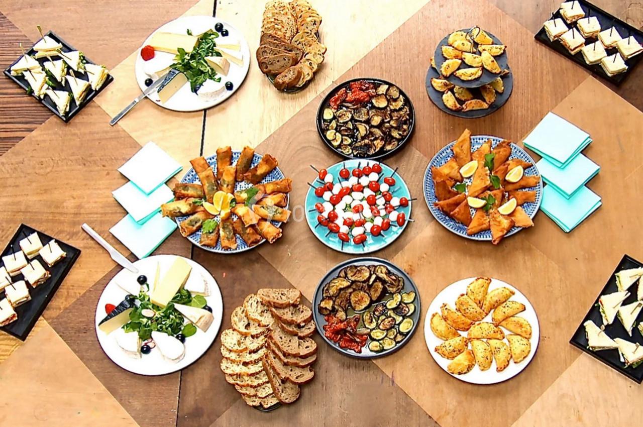 Assortiment de plats apéritifs disposés sur une table en bois, comprenant légumes grillés, pains, fromages et feuilletés.
