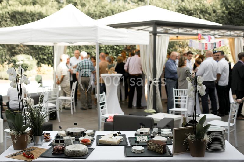 Table garnie de plateaux de fromages variés en premier plan, avec des invités discutant sous des tentes en arrière-plan.