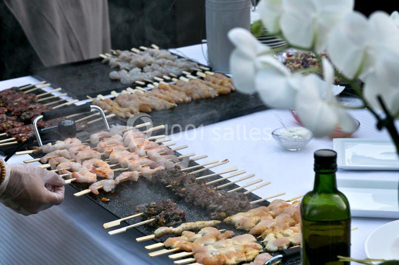 Brochettes de viande et de crevettes grillées sur des plaques chauffantes lors d'un buffet en extérieur.