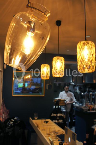 Lampes suspendues éclairant un comptoir dans un restaurant, avec un chef cuisinier en arrière-plan.