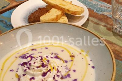 Une femme souriante se tient derrière un stand de produits variés dans une salle décorée avec un sapin de Noël.