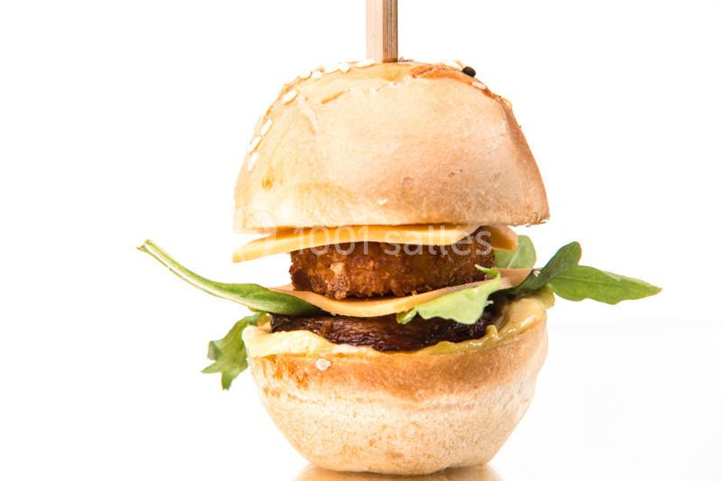 Mini burger garni de fromage, roquette, galette panée et sauce, présenté avec un pic en bois.