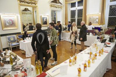 Une femme souriante se tient derrière un stand de produits variés dans une salle décorée avec un sapin de Noël.