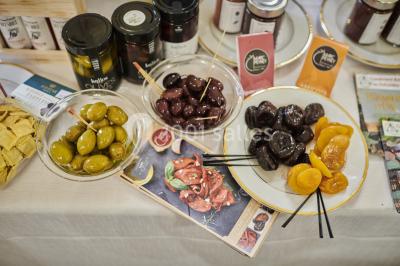 Une femme souriante se tient derrière un stand de produits variés dans une salle décorée avec un sapin de Noël.