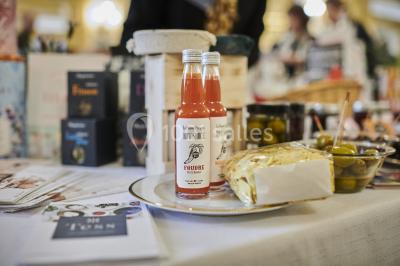 Une femme souriante se tient derrière un stand de produits variés dans une salle décorée avec un sapin de Noël.