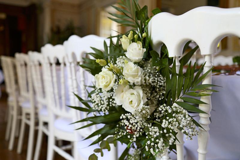 Chaises blanches décorées de fleurs blanches et de feuillage, alignées dans une salle lumineuse.