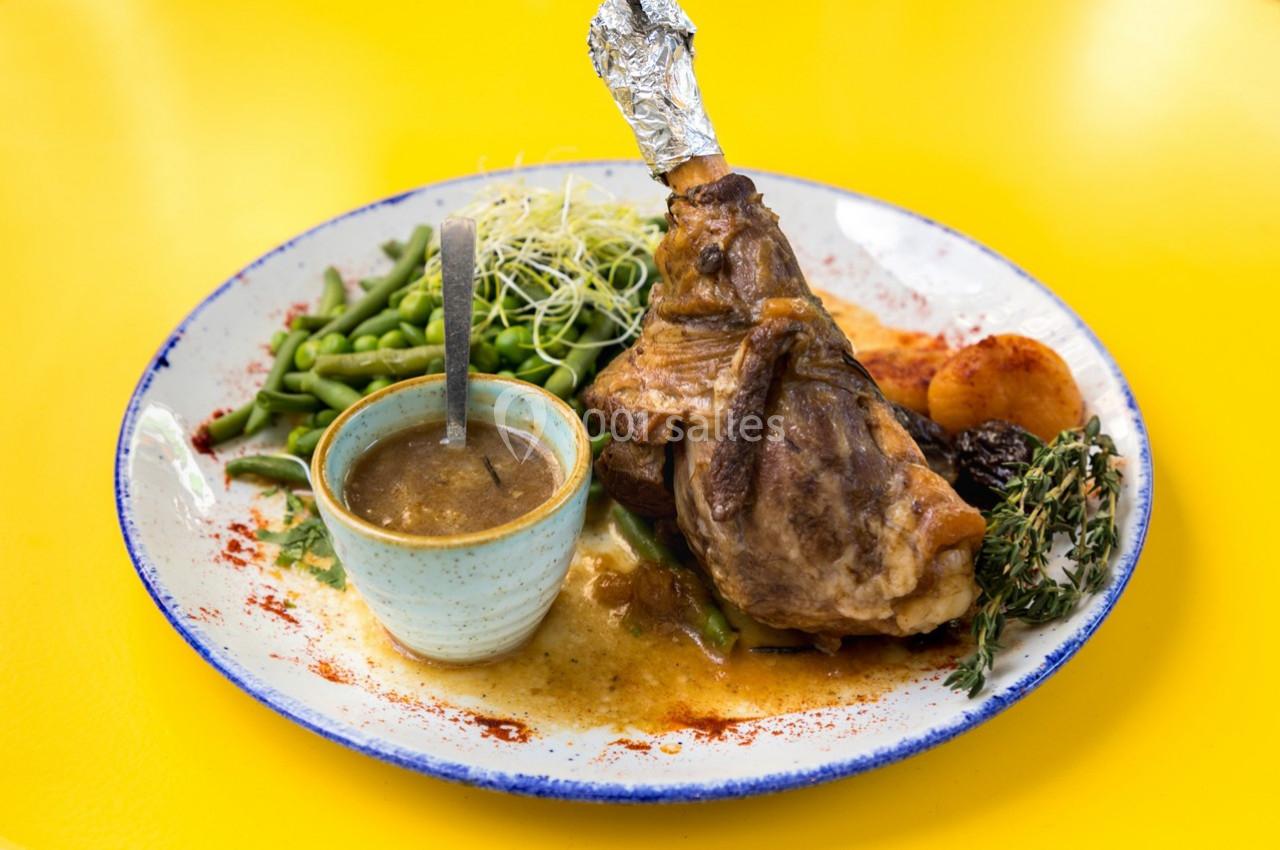 Assiette contenant un jarret d'agneau, haricots verts, pommes de terre, pruneaux, sauce et garniture d'herbes.