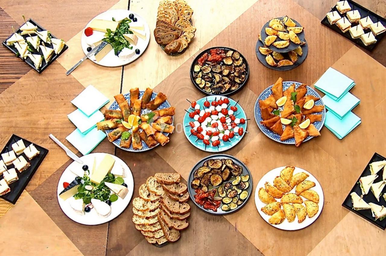 Assortiment de plats apéritifs variés disposés sur une table en bois, comprenant légumes, pains et amuse-bouches.