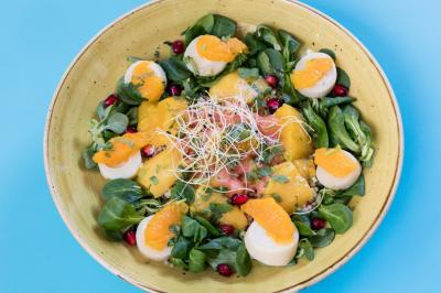 Une femme souriante se tient derrière un stand de produits variés dans une salle décorée avec un sapin de Noël.