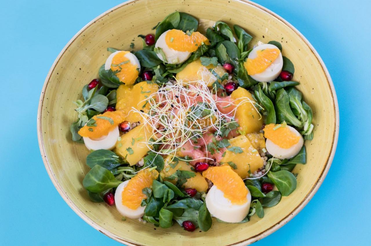 Salade colorée avec mâche, tranches d'orange, fromage, graines de grenade et germes sur une assiette jaune.