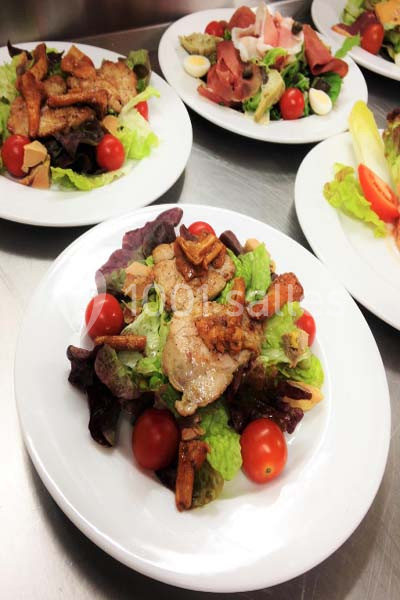 Assiette de salade garnie de feuilles vertes, tomates cerises, champignons et morceaux de viande grillée.