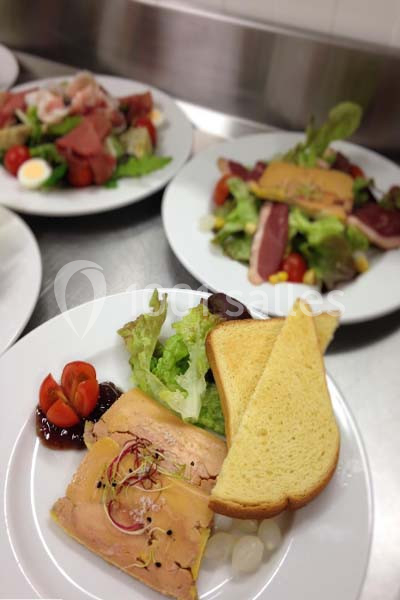 Assiette composée de foie gras, toasts, salade verte, tomates cerises et confiture, présentée sur une table.