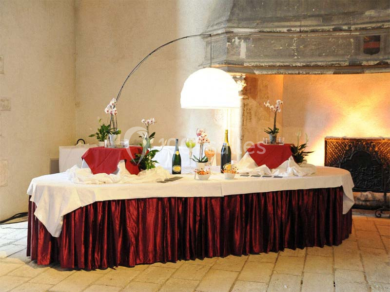 Table décorée avec nappes blanches et rouges, ornée de plantes et de bouteilles, dans une salle au mur en pierre.