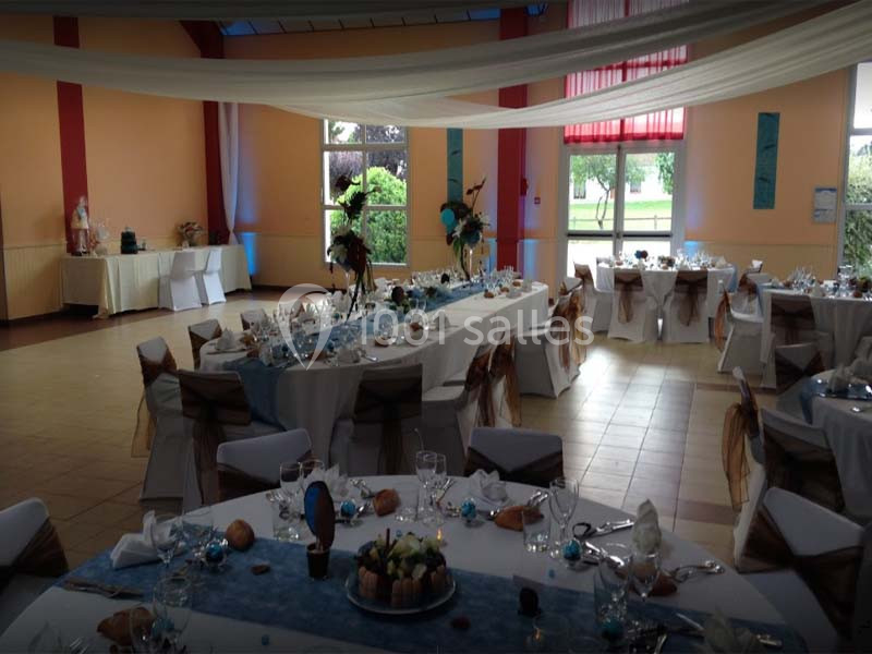 Salle de réception décorée avec des tables dressées, nappes blanches et touches de bleu, prête pour un événement.