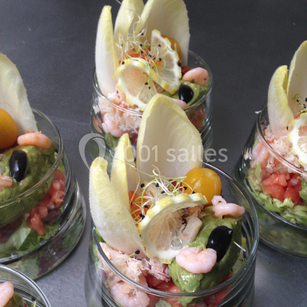 Verrines garnies de crevettes, avocat, tomates, endives, citron, olives noires et germes, présentées sur une table.