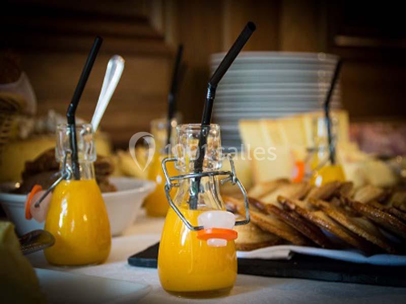 Bouteilles individuelles de jus d'orange avec pailles noires, entourées de viennoiseries et d'assiettes empilées.