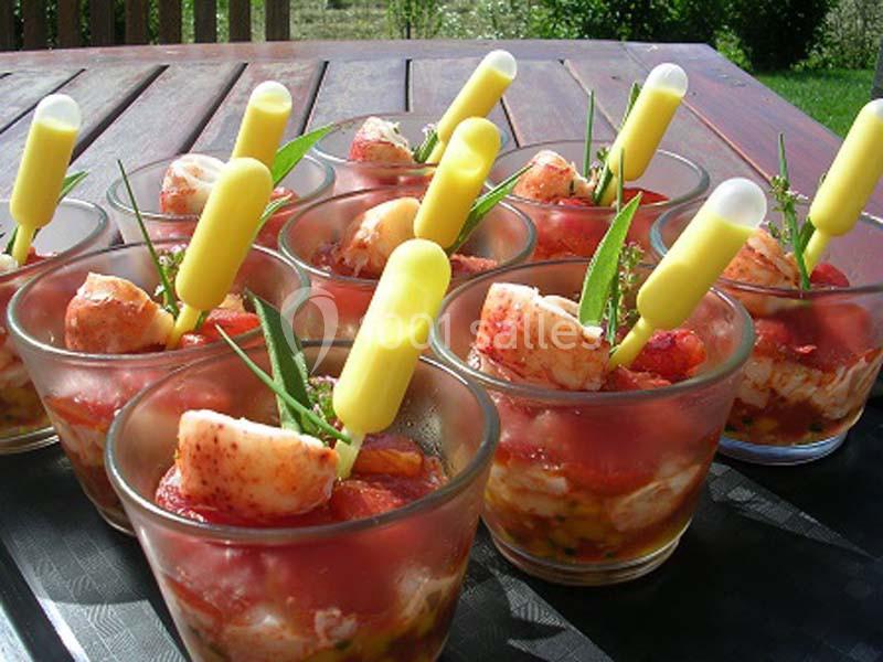 Verrines de homard avec pipettes de sauce, garnies de feuilles fraîches, présentées sur une table en extérieur.