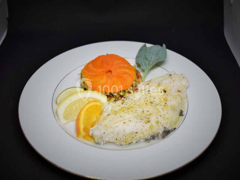 Assiette avec filet de poisson blanc, rondelle de citron, tranche d'orange et garniture de légumes colorés.