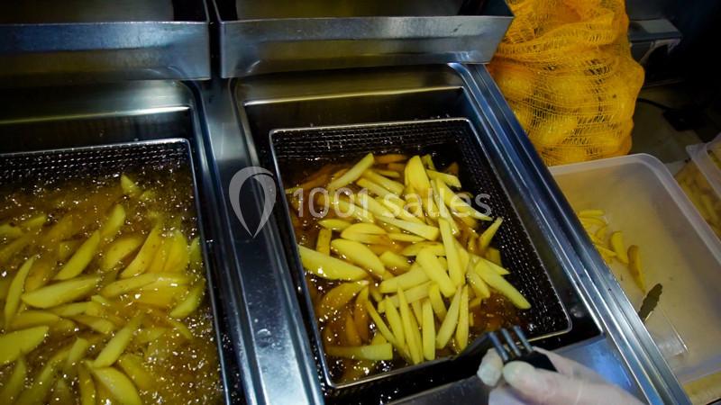 Frites en cours de cuisson dans une friteuse industrielle, avec des pommes de terre fraîches visibles à proximité.