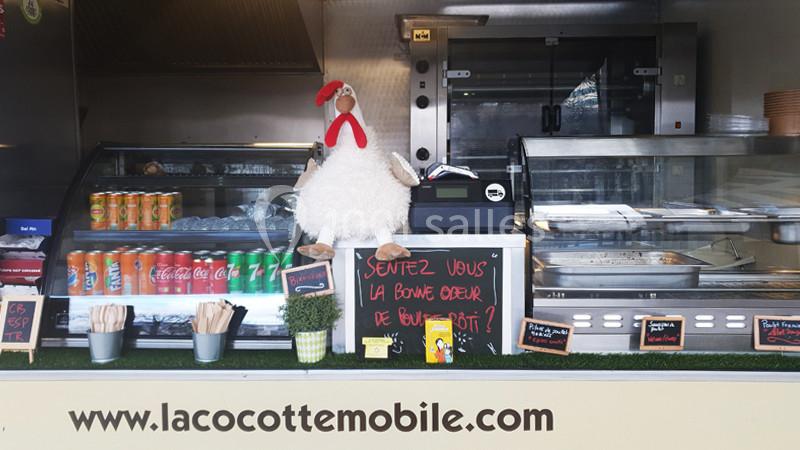 Un stand de restauration mobile avec une peluche de poule, des boissons en canettes et des plats exposés.