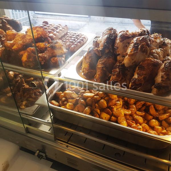 Poulets rôtis, saucisses et pommes de terre dorées exposés dans une vitrine de restauration.