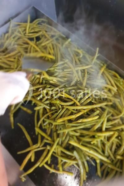 Haricots verts frais en train d’être sautés sur une plaque chaude, avec une main tenant une spatule.