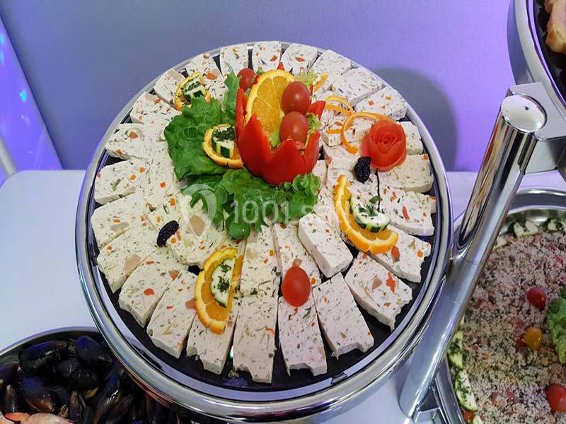 Plateau de terrine de volaille décoré de tranches d'orange, tomates cerises, laitue et fleurs sculptées en légumes.