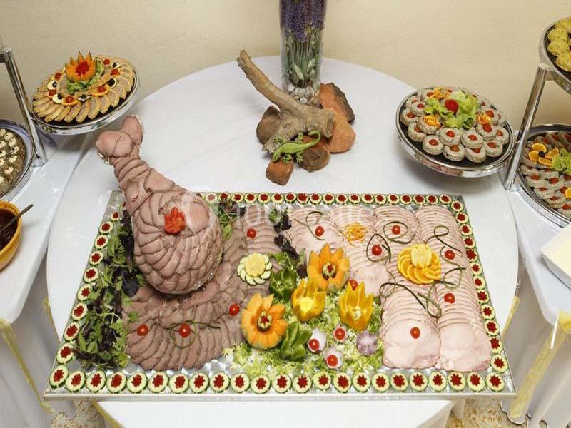Plateau de charcuterie décorative avec viandes tranchées, légumes sculptés et garnitures sur une table ronde.