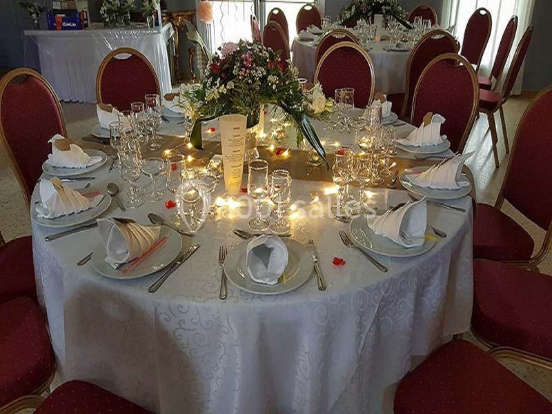Table ronde élégamment dressée avec nappes blanches, vaisselle, serviettes pliées, fleurs et lumières décoratives.