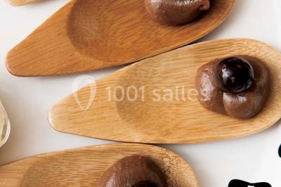 Salle de réception décorée avec des tables alignées, nappes blanches, chaises pliantes et ornements suspendus.