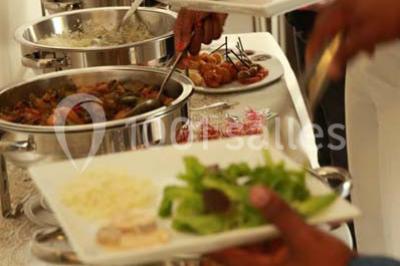 Salle de réception décorée avec des tables alignées, nappes blanches, chaises pliantes et ornements suspendus.