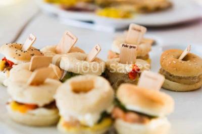 Salle de réception décorée avec des tables alignées, nappes blanches, chaises pliantes et ornements suspendus.