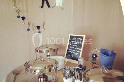 Salle de réception décorée avec des tables alignées, nappes blanches, chaises pliantes et ornements suspendus.