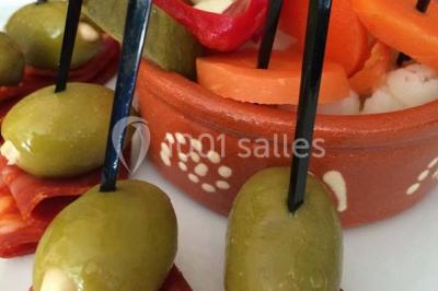 Salle de réception décorée avec des tables alignées, nappes blanches, chaises pliantes et ornements suspendus.