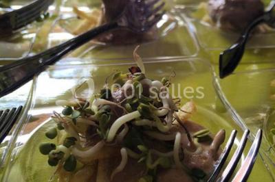 Salle de réception décorée avec des tables alignées, nappes blanches, chaises pliantes et ornements suspendus.